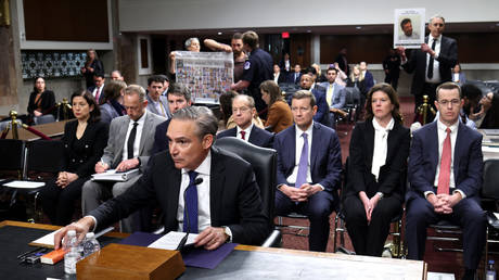 FILE PHOTO: Boeing CEO Kelly Ortberg testifies before a Senate committee as protesters hold signs depicting victims of 737 MAX crashes